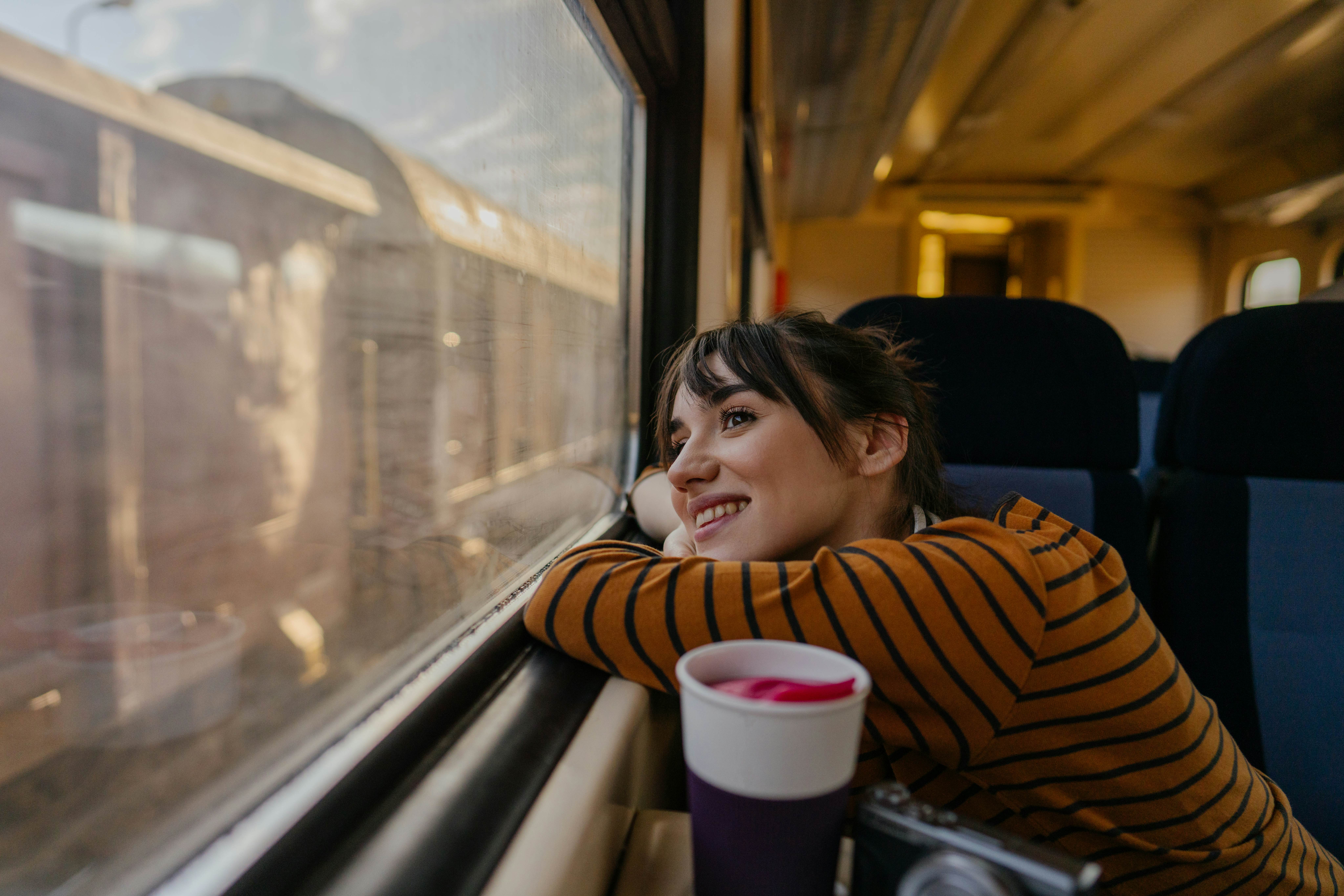 Photo of a young woman riding on a train, enjoying her trip while looking through the window